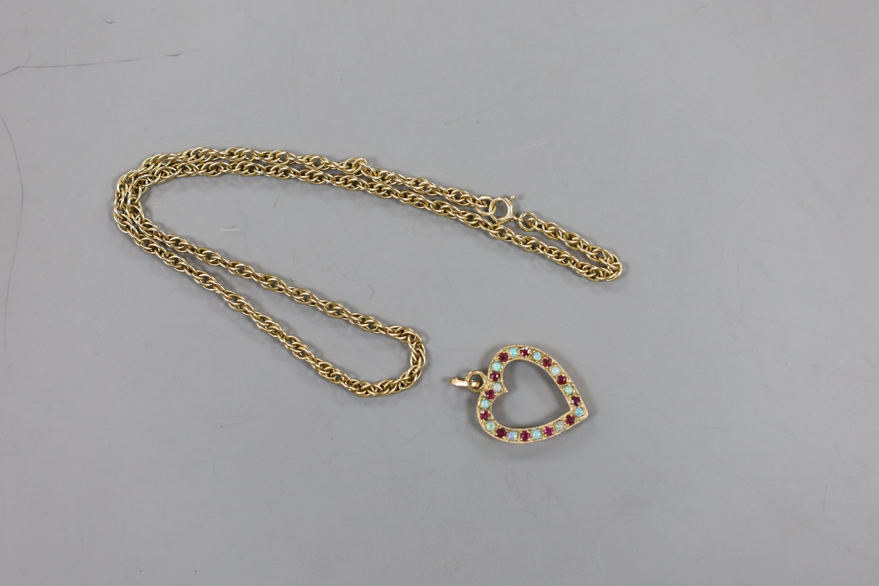 A modern 9ct gold, ruby and white opal set heart shaped open work pendant, 27mm and a 9ct gold chain, 38cm, gross weight 10.1 grams.